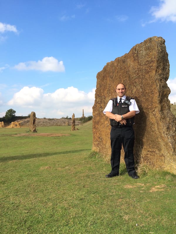 Andy Stuart in his police uniform leaning on a large upright stone from Ham Hill Stone Circle