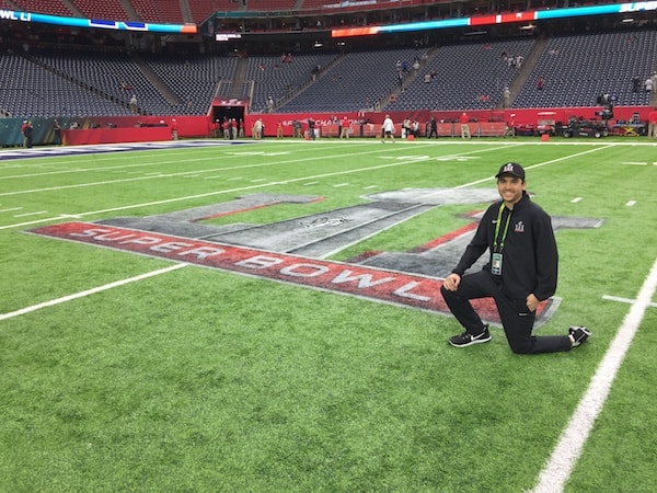 McLaughlin poses in front of the Super Bowl Logo painted on the field of NRG Stadium