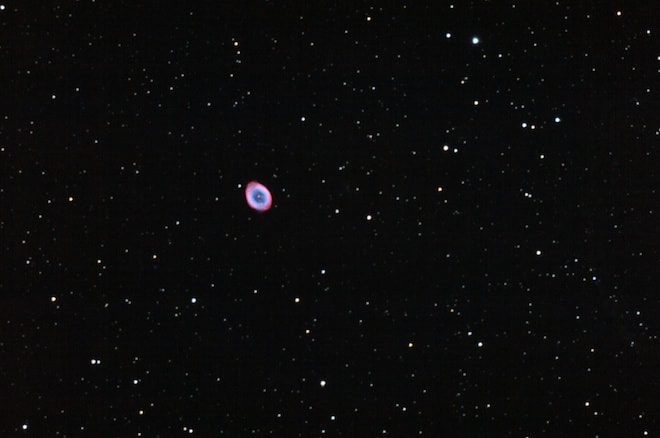 A small purple and blue cloud among a pitch black sky with dozen tiny stars.