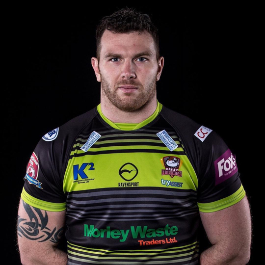 Keegan Hirst stands againsts a black background, arms behind his back, wearing his rugby uniform.