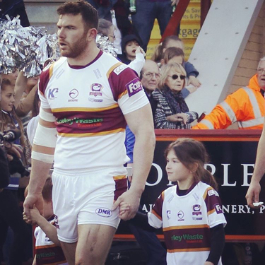 Hirst walking on a rugby field while holding two children's hands. They are wearing matching uniforms.