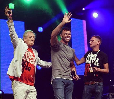 Hirst stands on stage next to Ian McKellen and waves to the crowd.