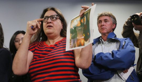 A reporter points to a photo while asking someone offscreen a question.