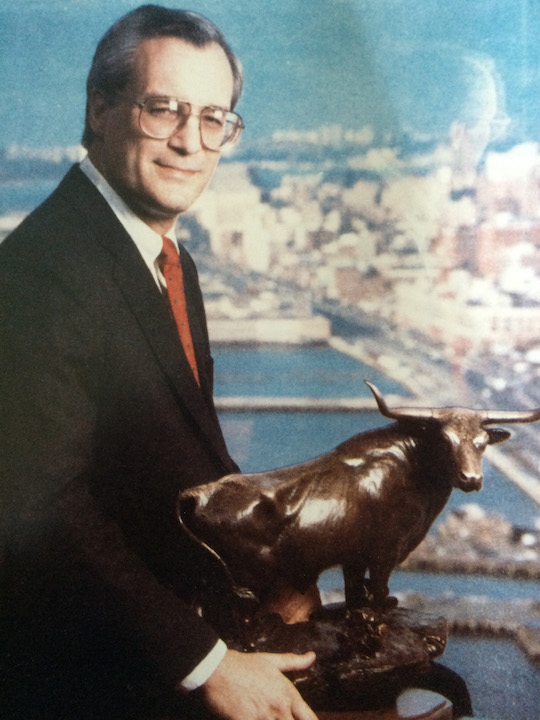 An official portrait of Paul Critchlow holding a Wall Street bull with the New York skyline in the background.