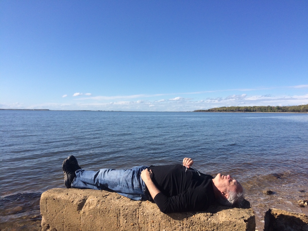 Paul is on his back relaxing on a clear and isolated beach.
